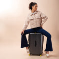 Stylish woman sitting on Trunk Check-In Plus luggage, showcasing modern travel.