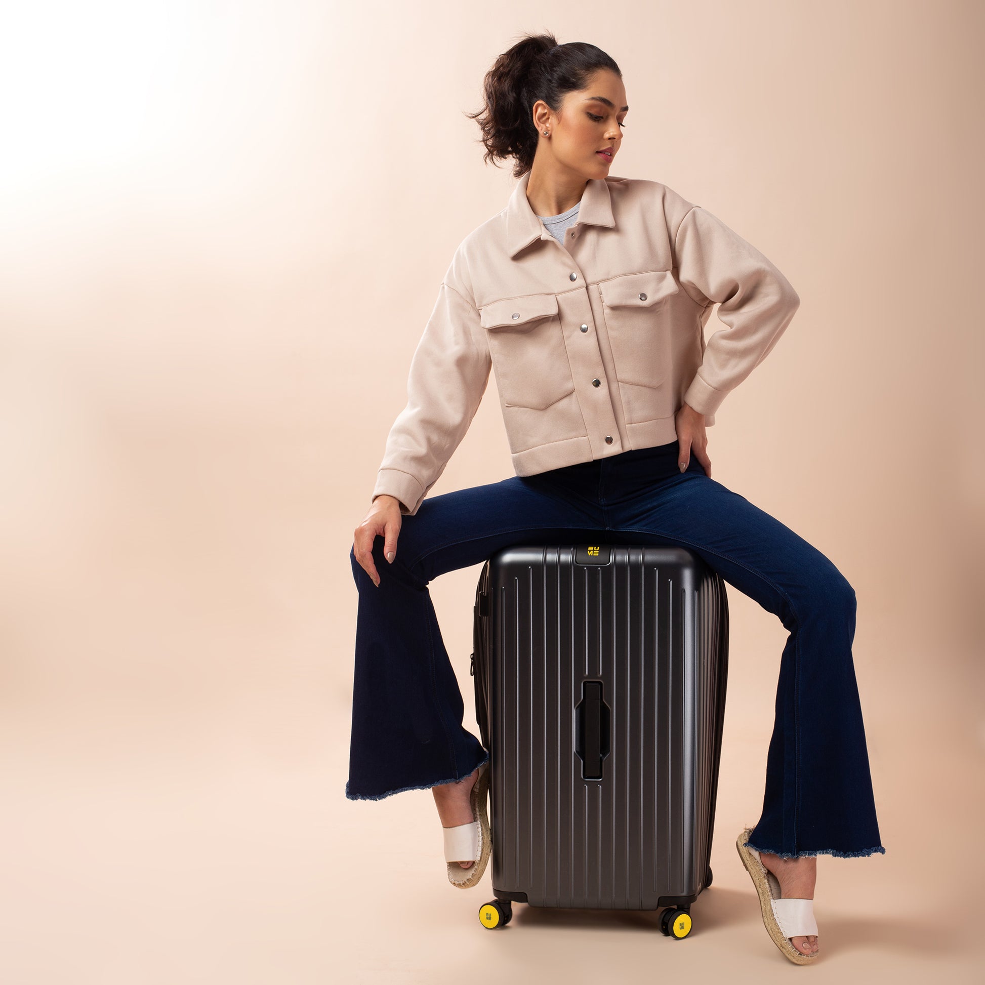 Stylish woman sitting on Trunk Check-In Plus luggage, showcasing modern travel.