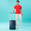 Man in red polo with navy cabin suitcase on turquoise background.