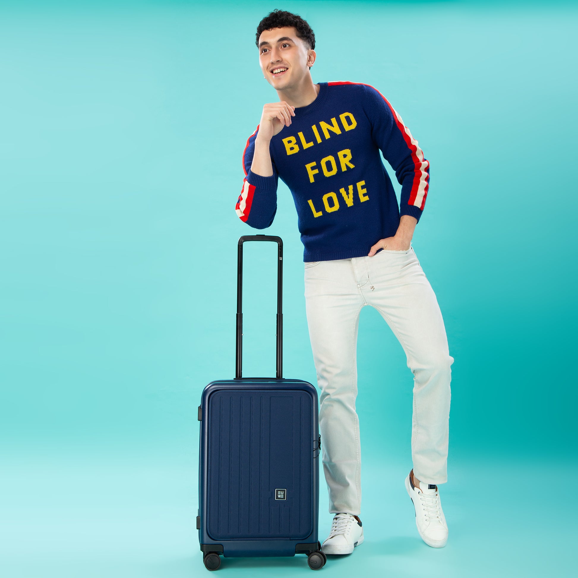 Man in sweater posing with Cabin Pro suitcase on turquoise background.