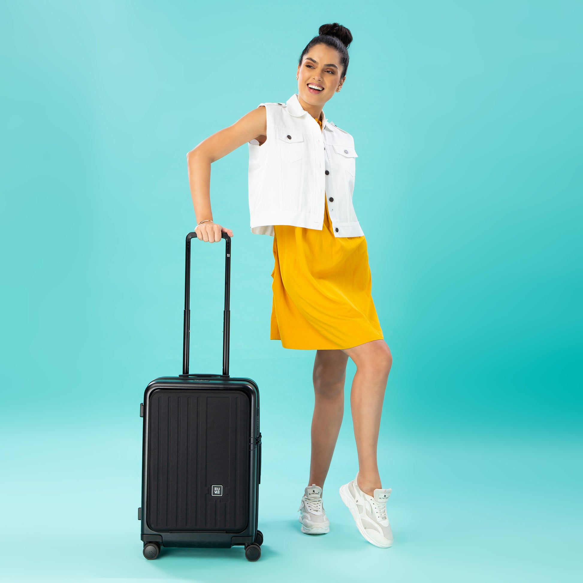 Woman posing with Cabin Pro luggage on a turquoise background.