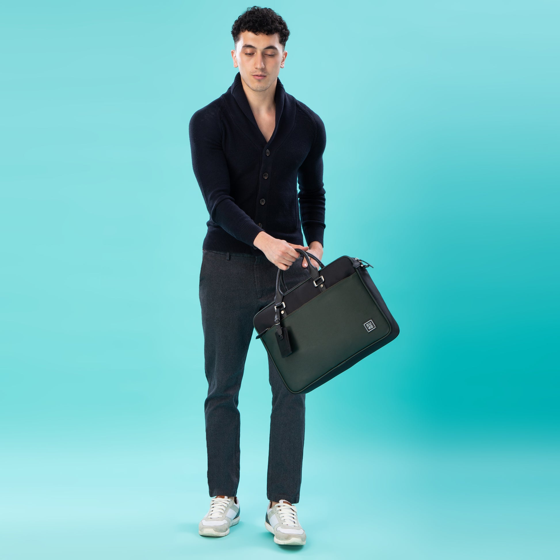 Stylish man holding Commute Messenger Bag against a teal background.