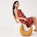 Cinnamon hobo bag styled with elegant attire on model.