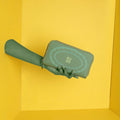 EUME Bandwing Clutch in stylish green hand against yellow background.