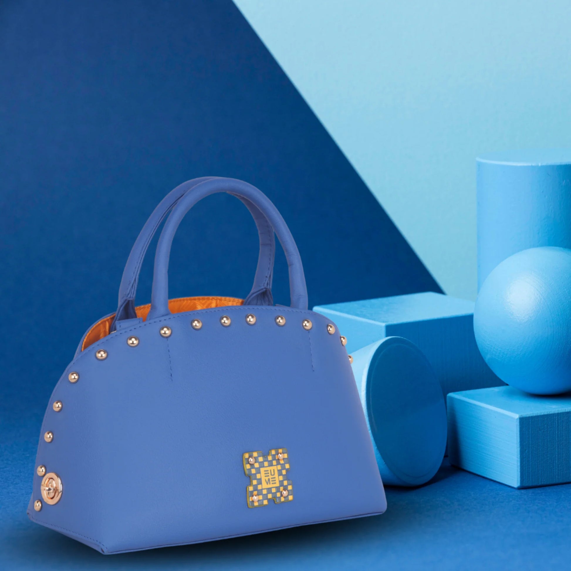 Stylish blue marigold satchel bag with studs on blue background.