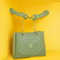 Green Flapper Laptop Handbag being held against a vibrant yellow background.